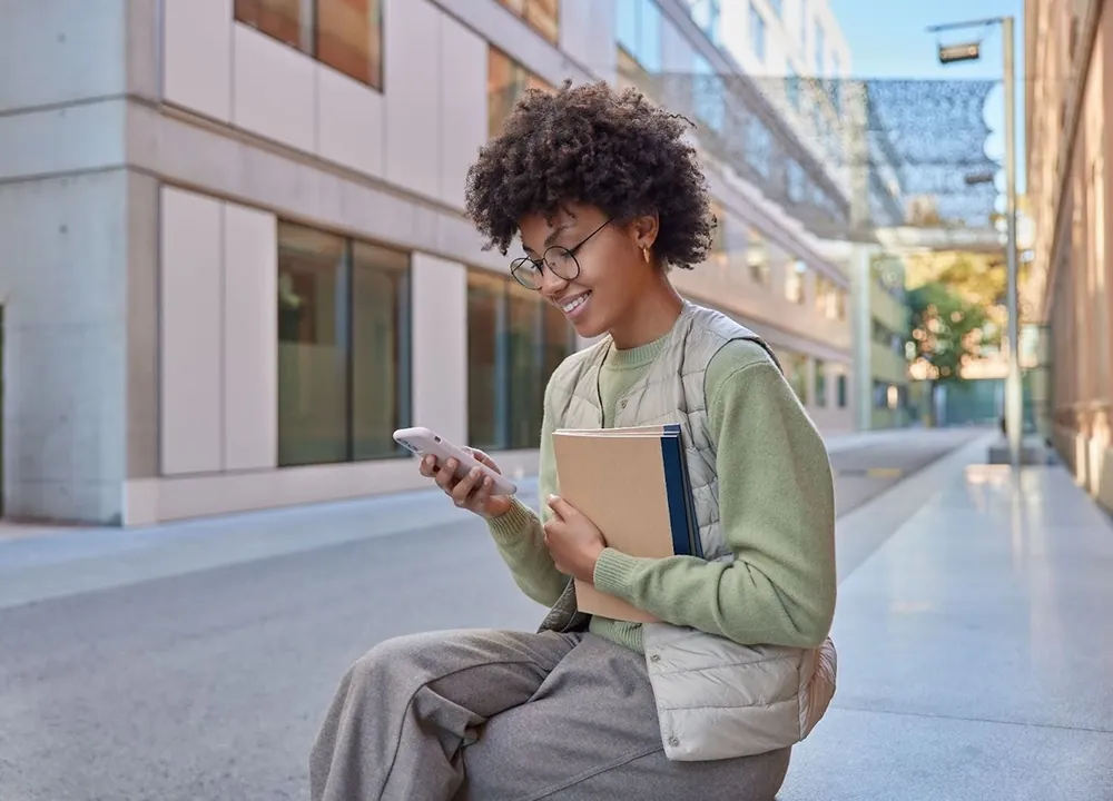 Student sitting outside a college building, using a free government smartphone